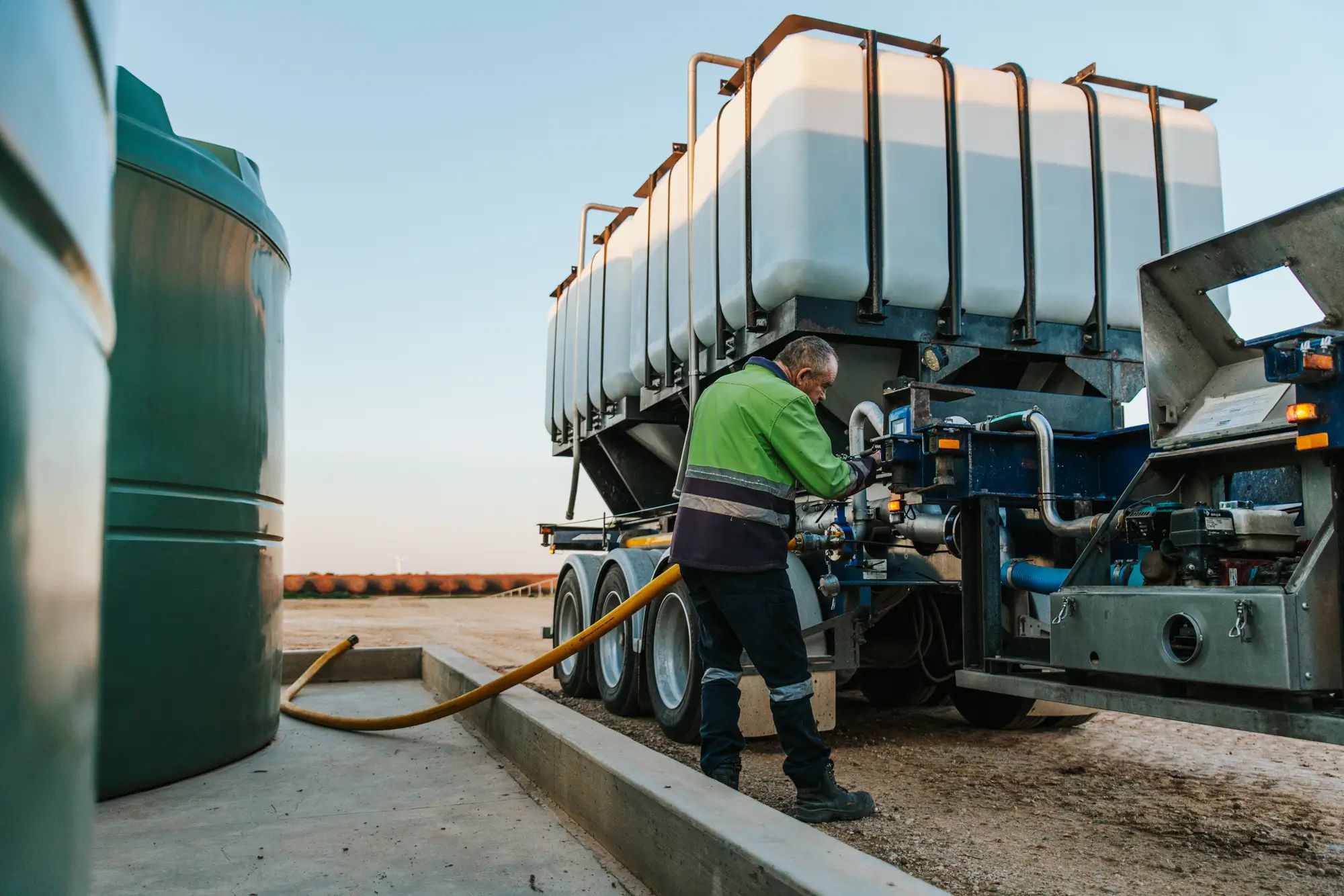Worker filling a tank on an Australian farm using liquid fertiliser, enhancing soil nutrition for higher fruit yields with NuEdge products.